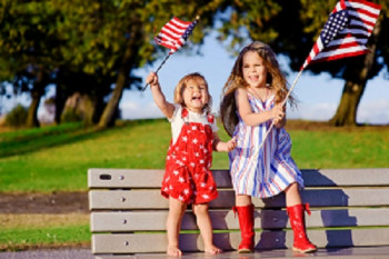 Picture of two happy kids waving the American flag on a bench.